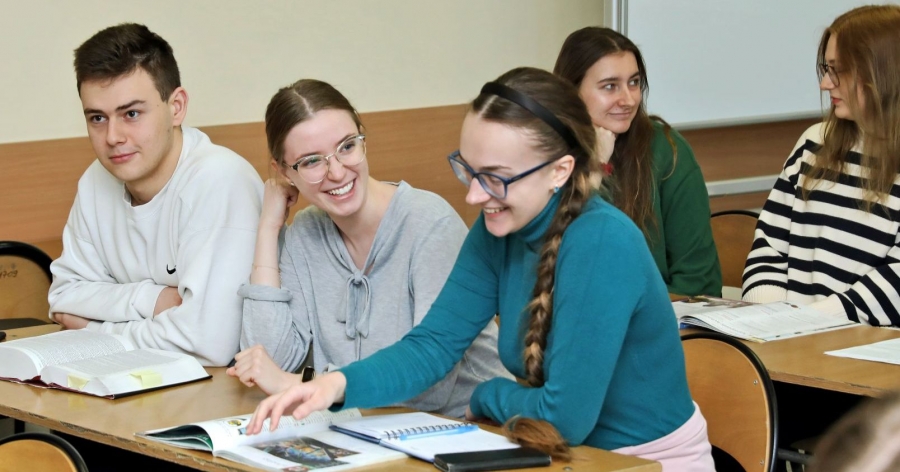 Studenci podczas zajęć, przed nimi na stołach leżą otwarte książki i zeszyty