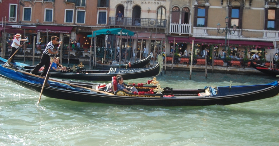 Łódka na kanale wodnym w Wenecji z wioślarzami i turystami.