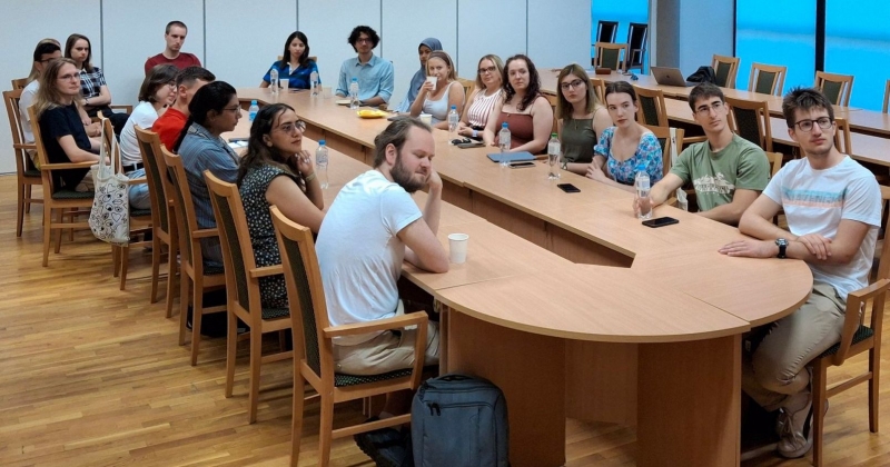 Grupa studentów, uczestników programu letniego, siedzi przy owalnym stole i słuchają wykładu, ich głowy skierowane są w stronę prelegentów, których nie widać na zdjęciu
