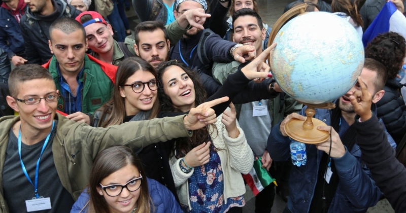 One person holds the globe and other people point fingers at different places on the globe