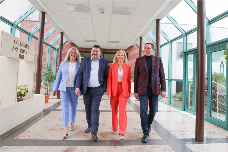 Four people: 2 women and 2 men walking down a bright corridor. 