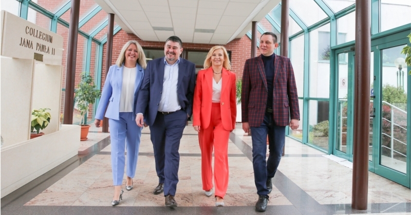 Four people: 2 women and 2 men walking down a bright corridor. 