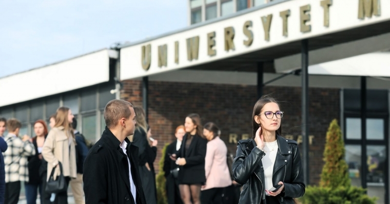 Grupa osób stojących przed budynkiem Uniwersytetu