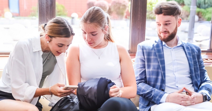 Studentka pokazuje coś na ekranie telefonu swojej koleżance i koledze.