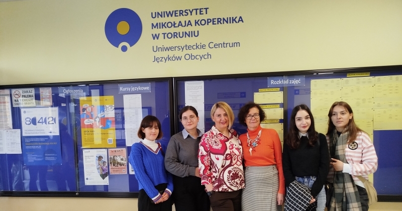 In the foreground, students and lecturers of English are standing in a row, smiling. In the background, above the heads of the students, there is an inscription: University Centre for Foreign Languages