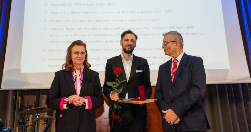 Prof. Karwacki na scenie razem z przedstawicielami kapituły konkursu. W rękach trzyma dyplom, medal i różę