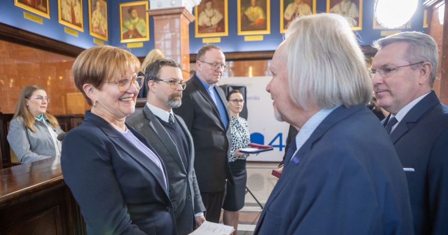 Rektor wręcza odznaczenie prof. Magdalenie Osińskiej. Obok rektora wicewojewoda, w kolejce stooją następne osoby, które otrzymają medal. w tle portrety rektorów UMK w reprezentacyjnej sali senatu Collegium Maximum